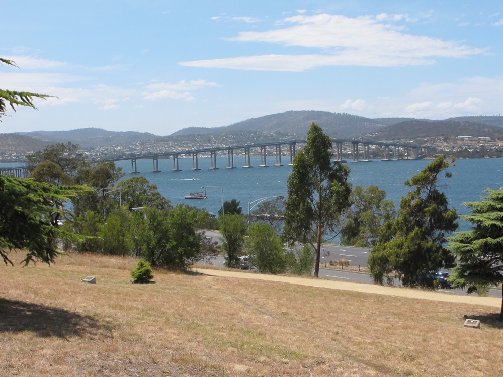 Plaques visible in the brown grass, Tasman bridge behind.